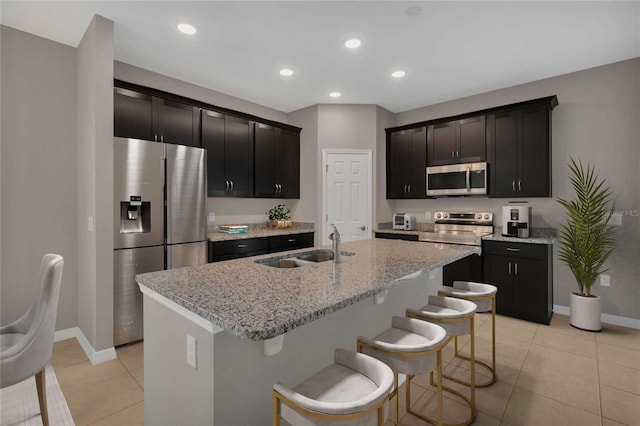 kitchen featuring sink, a breakfast bar area, light stone counters, stainless steel appliances, and a kitchen island with sink