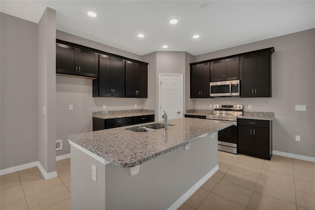 kitchen featuring light tile patterned floors, sink, stainless steel appliances, light stone countertops, and a center island with sink