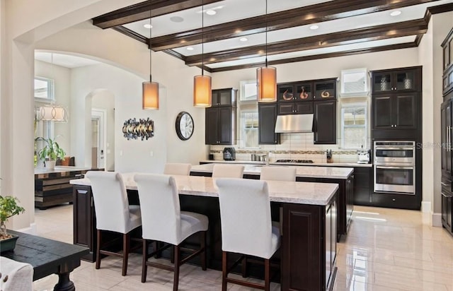 kitchen with hanging light fixtures, double oven, a center island, and backsplash