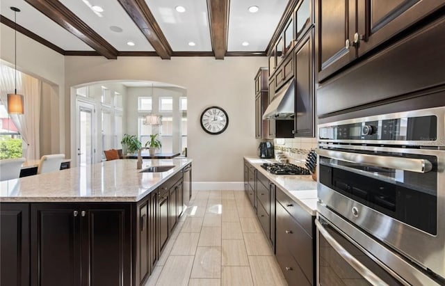 kitchen with hanging light fixtures, beam ceiling, sink, and a kitchen island with sink