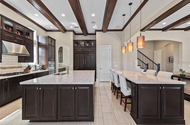 kitchen with light stone countertops, backsplash, hanging light fixtures, a large island, and light tile floors