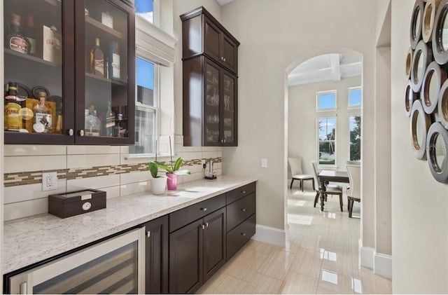 kitchen with dark brown cabinets, beverage cooler, tasteful backsplash, light stone counters, and light tile floors