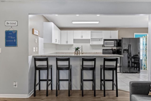 kitchen featuring black appliances, a kitchen bar, white cabinetry, and kitchen peninsula