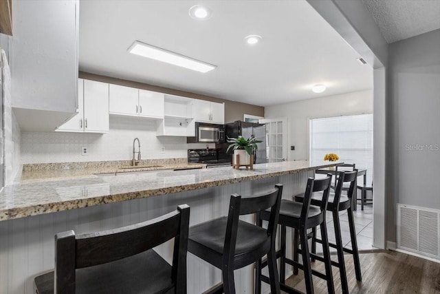 kitchen featuring a breakfast bar, black appliances, kitchen peninsula, light stone countertops, and white cabinetry