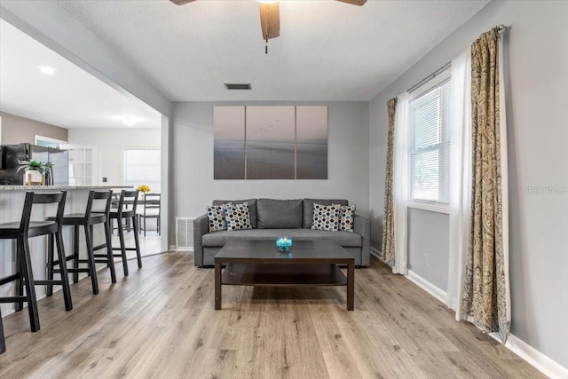 living room with ceiling fan, light hardwood / wood-style floors, and a textured ceiling