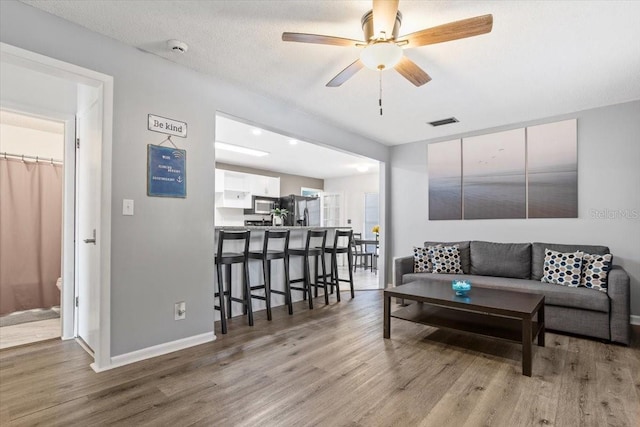 living room with ceiling fan, light hardwood / wood-style floors, and a textured ceiling