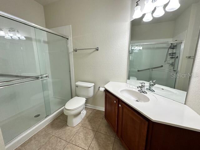 bathroom featuring tile floors, a shower with door, vanity with extensive cabinet space, and toilet