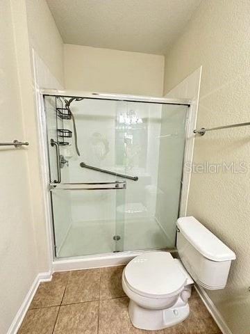 bathroom with an enclosed shower, tile flooring, toilet, and a textured ceiling