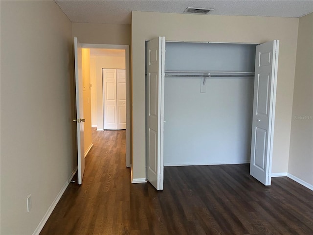 unfurnished bedroom featuring a textured ceiling, a closet, and dark wood-type flooring