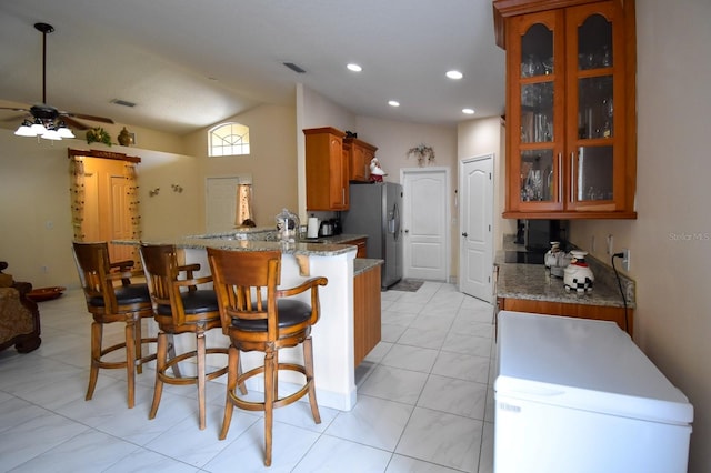 kitchen with stone counters, kitchen peninsula, ceiling fan, vaulted ceiling, and light tile floors