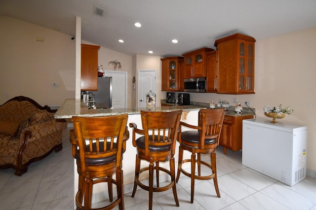 kitchen with kitchen peninsula, stainless steel appliances, light tile floors, and light stone countertops