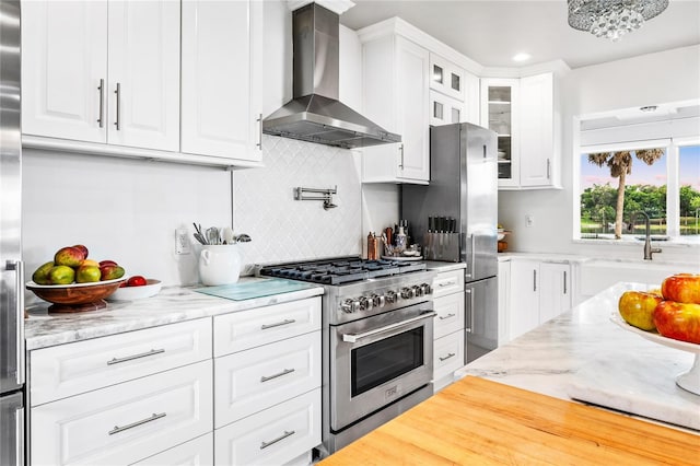 kitchen featuring hardwood / wood-style floors, tasteful backsplash, wall chimney range hood, white cabinetry, and appliances with stainless steel finishes