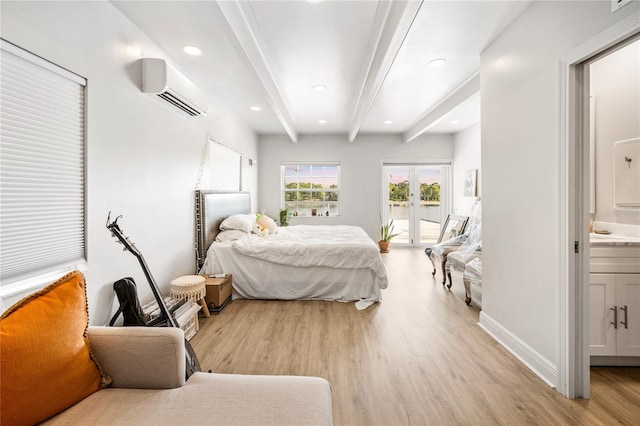 bedroom with beamed ceiling, light wood-type flooring, a wall unit AC, access to exterior, and connected bathroom