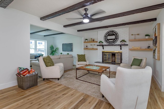 living room with beamed ceiling, ceiling fan, a fireplace, and light hardwood / wood-style floors