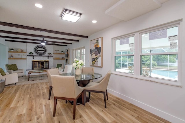 dining area featuring ceiling fan, a fireplace, beam ceiling, and light wood-type flooring