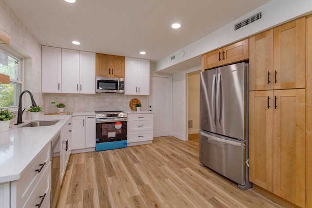 kitchen with sink, light hardwood / wood-style flooring, appliances with stainless steel finishes, tasteful backsplash, and white cabinets