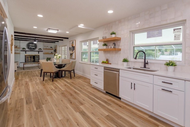 kitchen featuring sink, appliances with stainless steel finishes, a fireplace, light hardwood / wood-style floors, and white cabinets