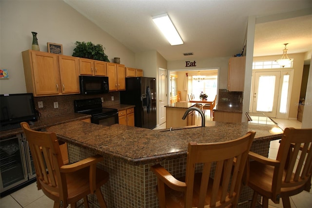 kitchen featuring tasteful backsplash, lofted ceiling, black appliances, kitchen peninsula, and a kitchen breakfast bar