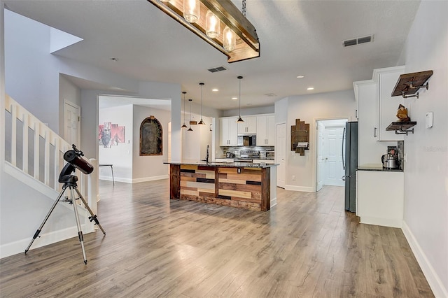 kitchen featuring stainless steel refrigerator, hanging light fixtures, white cabinets, and hardwood / wood-style floors