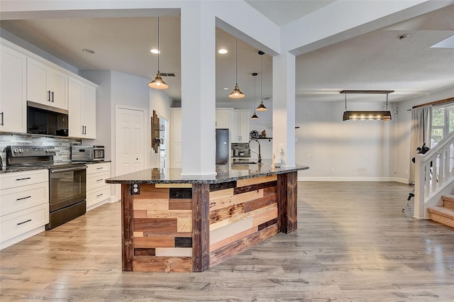 kitchen featuring decorative light fixtures, appliances with stainless steel finishes, light hardwood / wood-style flooring, backsplash, and dark stone countertops