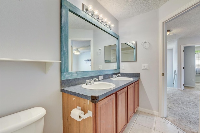 bathroom with tile flooring, ceiling fan, a textured ceiling, double vanity, and toilet