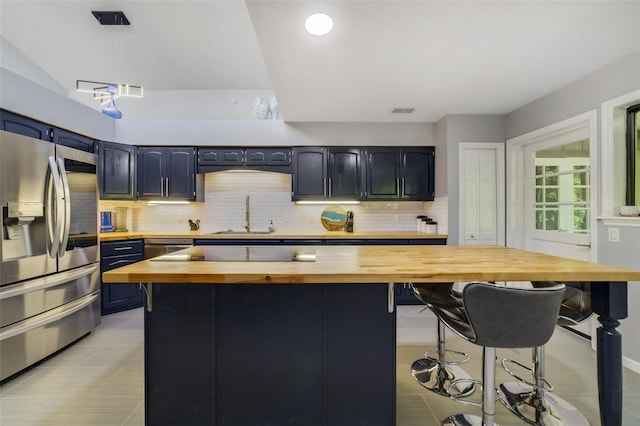 kitchen with wood counters, blue cabinets, sink, stainless steel fridge with ice dispenser, and a breakfast bar area