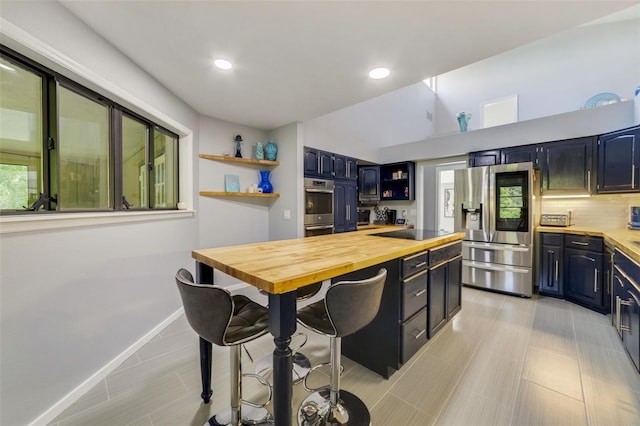 kitchen featuring appliances with stainless steel finishes, tasteful backsplash, blue cabinetry, butcher block countertops, and a breakfast bar area