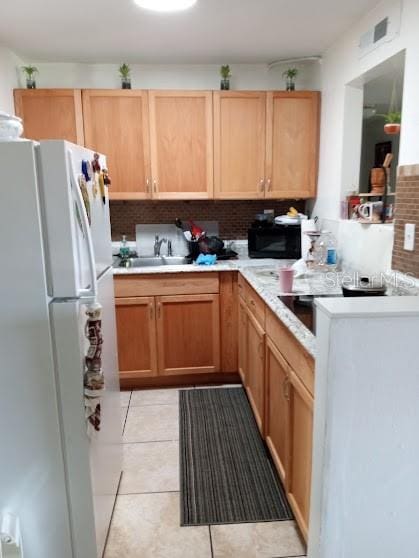 kitchen featuring backsplash, white refrigerator, sink, and light tile floors