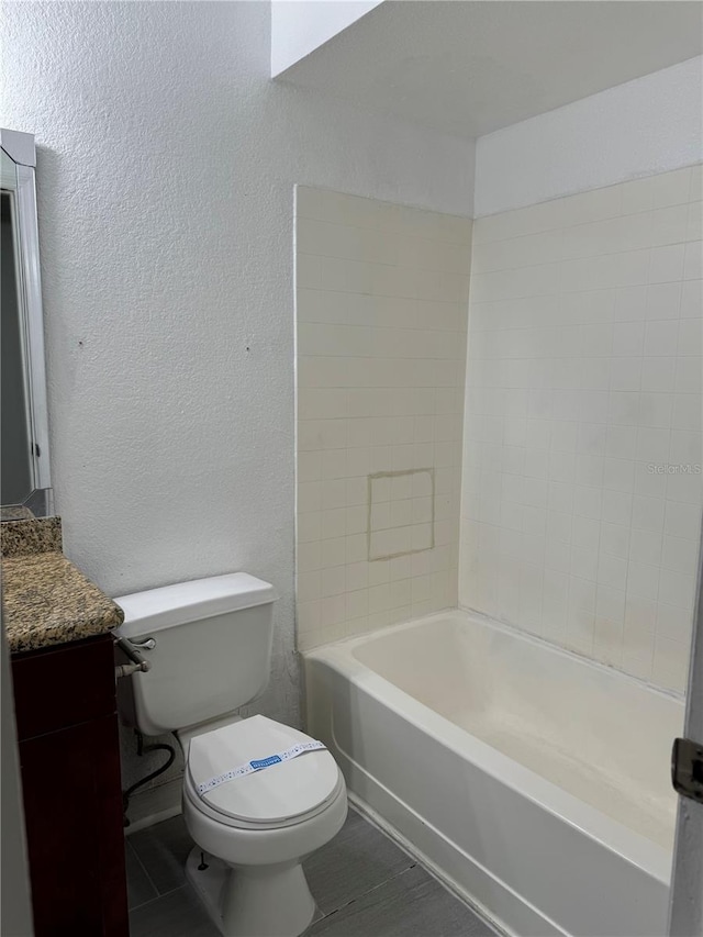 bathroom featuring a textured wall, bathing tub / shower combination, vanity, and toilet