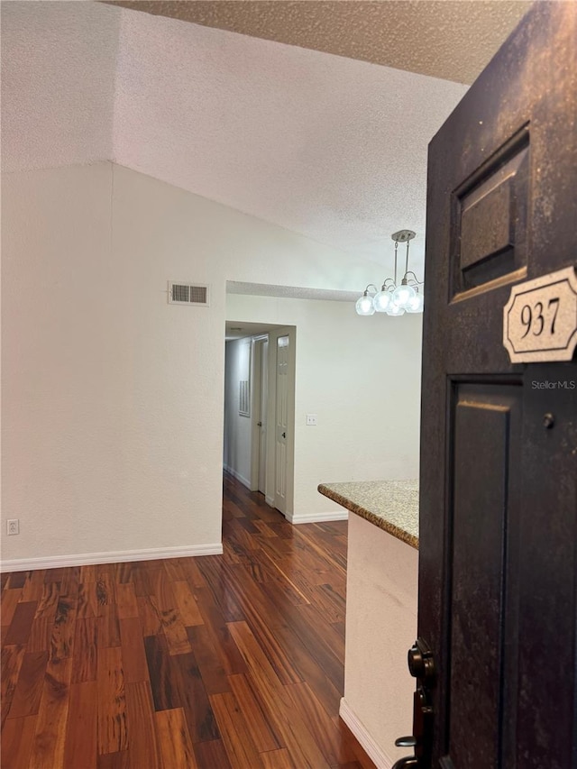 hall with lofted ceiling, a textured ceiling, visible vents, and dark wood-style flooring