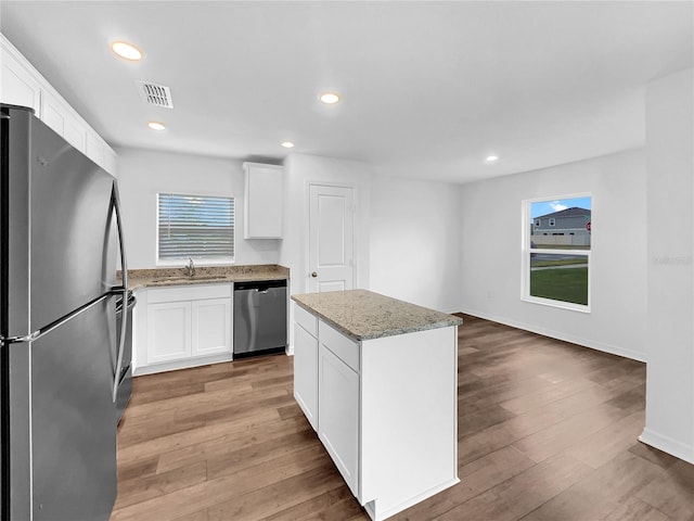 kitchen with appliances with stainless steel finishes, hardwood / wood-style floors, a kitchen island, and white cabinets