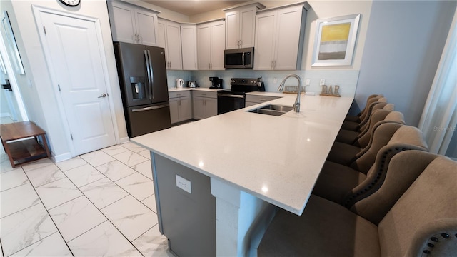 kitchen with black refrigerator with ice dispenser, range with electric cooktop, a breakfast bar area, gray cabinets, and sink