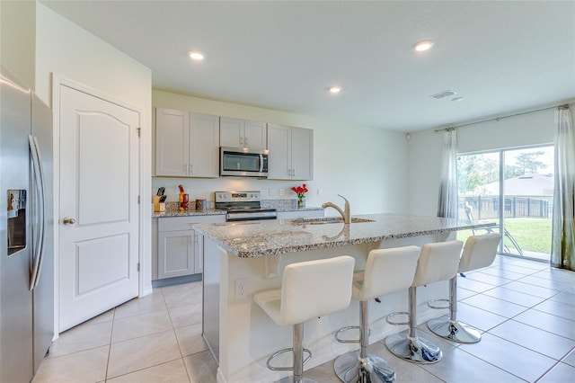 kitchen with appliances with stainless steel finishes, light tile flooring, a kitchen island with sink, sink, and a breakfast bar