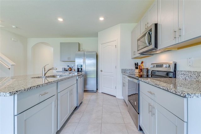 kitchen featuring sink, stainless steel appliances, an island with sink, and light stone counters