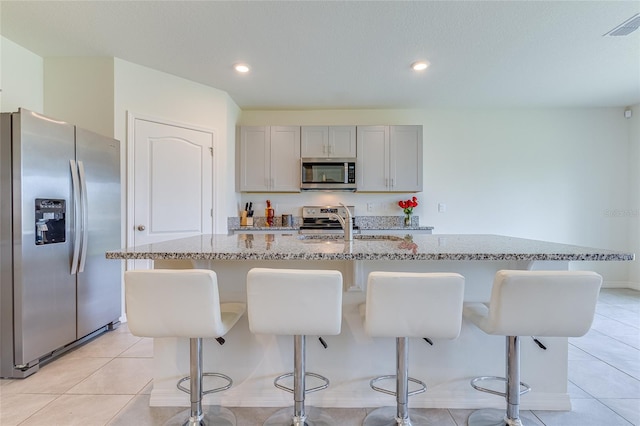 kitchen featuring appliances with stainless steel finishes, light tile floors, a center island with sink, and a breakfast bar area