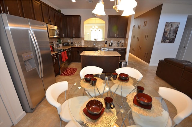 kitchen with appliances with stainless steel finishes, a kitchen island, backsplash, and light tile floors