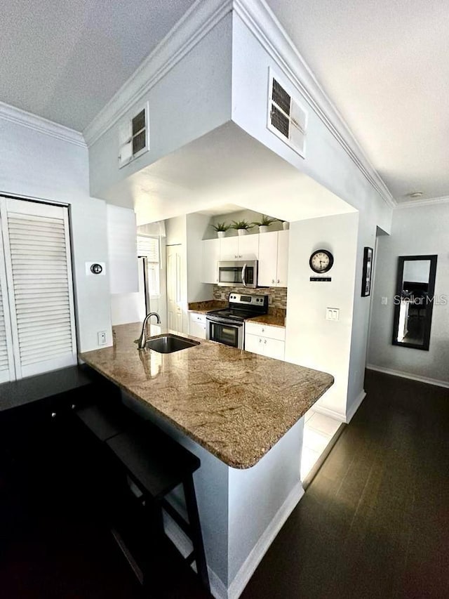 kitchen with white cabinetry, kitchen peninsula, appliances with stainless steel finishes, and a kitchen breakfast bar