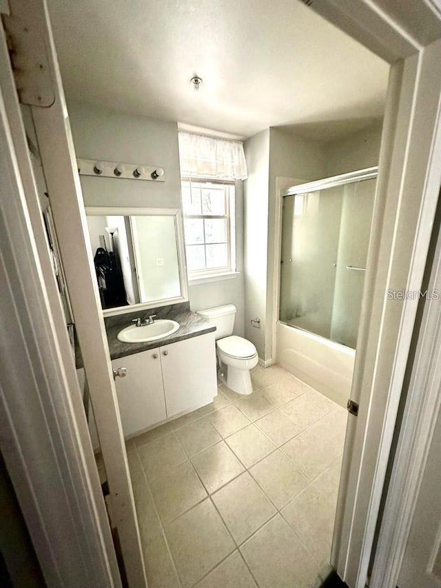 full bathroom featuring shower / bath combination with glass door, vanity, tile patterned floors, and toilet