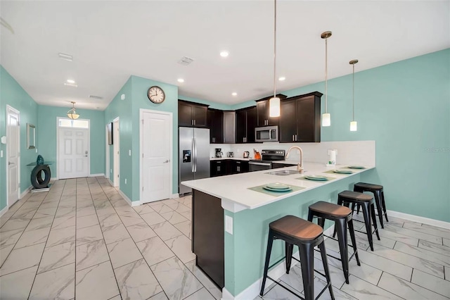 kitchen featuring hanging light fixtures, a breakfast bar, appliances with stainless steel finishes, dark brown cabinets, and sink