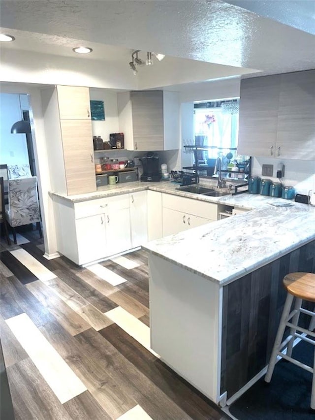 kitchen with sink, light stone counters, wood-type flooring, a breakfast bar, and white cabinets