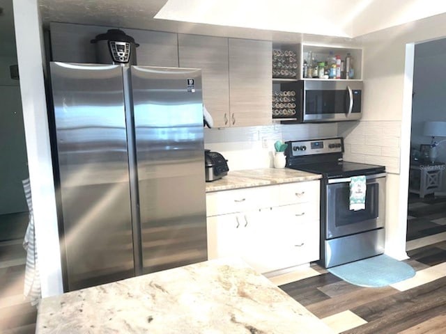 kitchen with appliances with stainless steel finishes, tasteful backsplash, light stone counters, and dark wood-type flooring