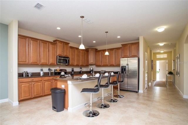 kitchen with appliances with stainless steel finishes, a breakfast bar, dark stone counters, an island with sink, and pendant lighting