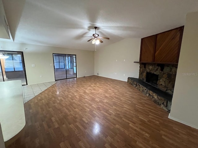 unfurnished living room with a stone fireplace, ceiling fan, vaulted ceiling, and dark hardwood / wood-style flooring