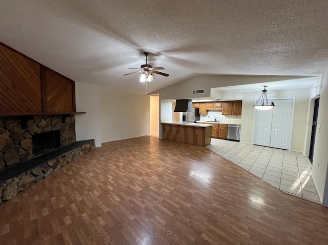 unfurnished living room with a fireplace, ceiling fan, light tile floors, sink, and a textured ceiling