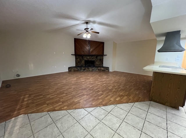 unfurnished living room with ceiling fan, a fireplace, and light tile floors