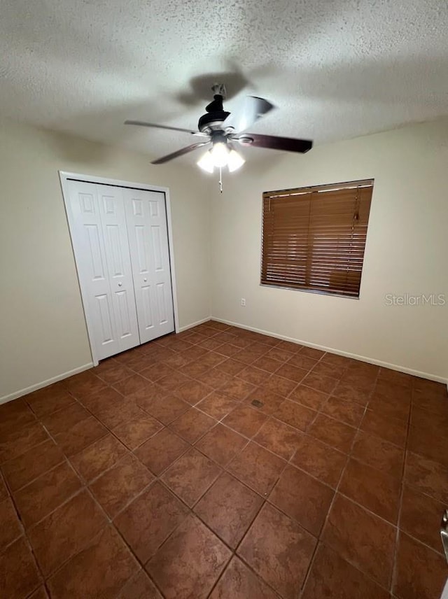 unfurnished bedroom with ceiling fan, a closet, a textured ceiling, and dark tile floors