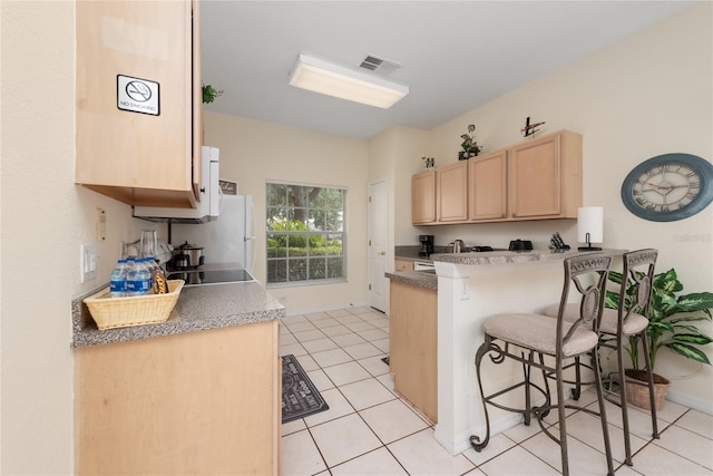 kitchen featuring light tile floors, kitchen peninsula, a breakfast bar, sink, and light brown cabinetry