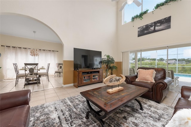 tiled living room with a towering ceiling and ceiling fan with notable chandelier