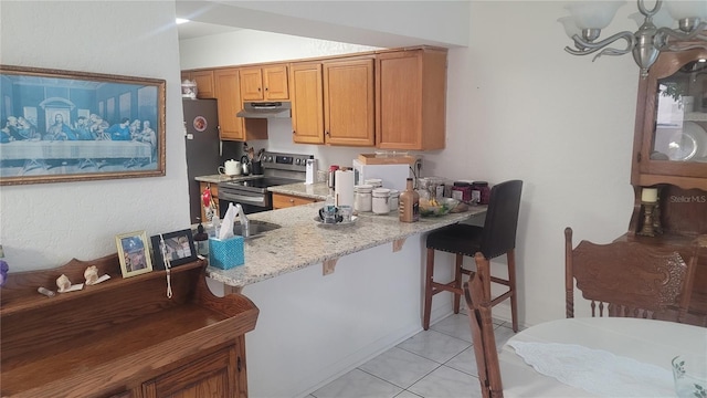 kitchen with black fridge, stainless steel range with electric stovetop, light tile patterned flooring, a kitchen bar, and light stone counters