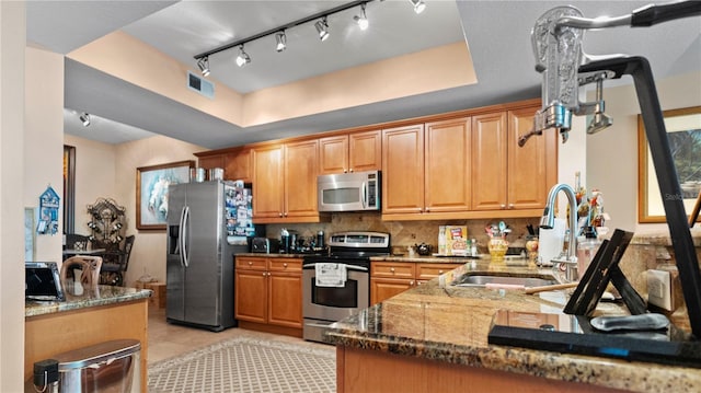 kitchen featuring appliances with stainless steel finishes, dark stone counters, sink, a raised ceiling, and kitchen peninsula